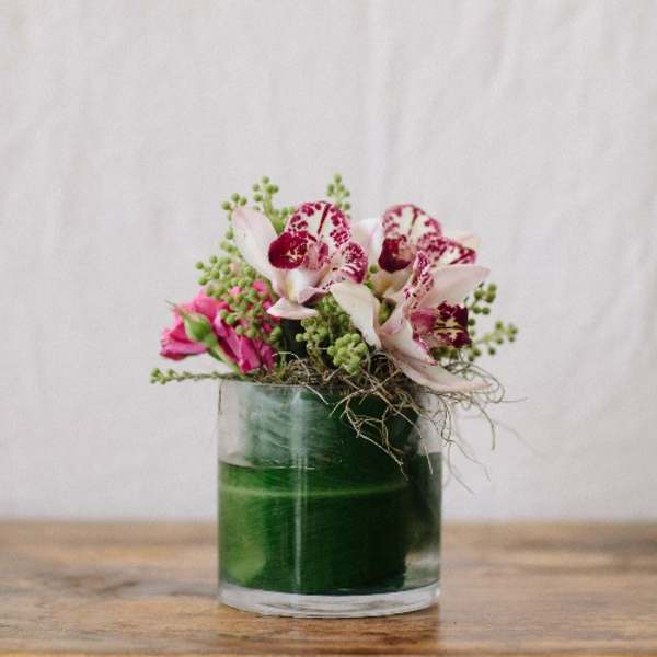 Pink and white orchids arranged in a green glass vase