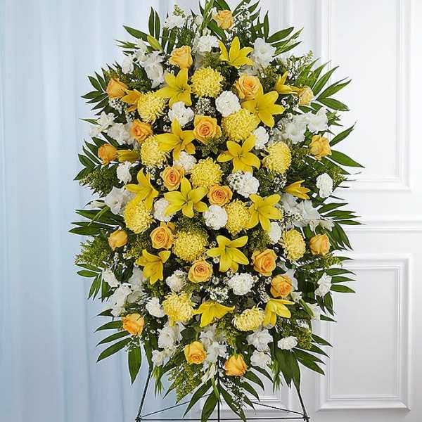 Tall standing spray of yellow lilies, yellow roses, and white flowers on an easel