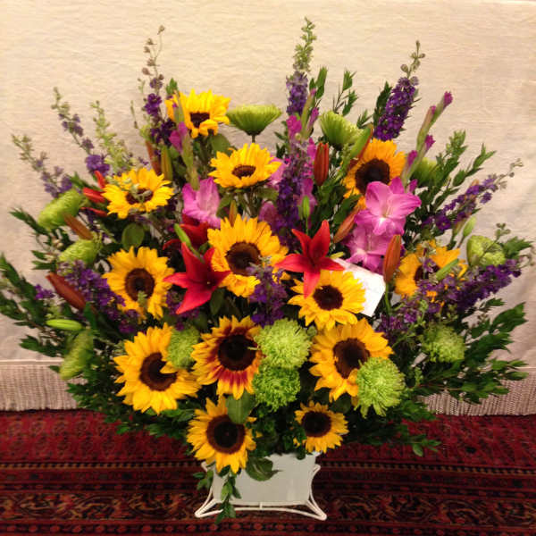 Large mixed bouquet with sunflowers, lilies, and purple flowers in a white container