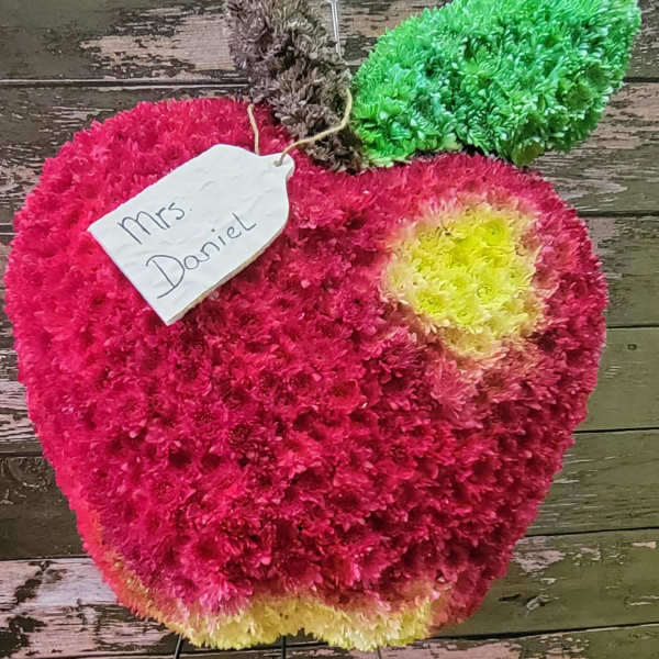 Apple-shaped floral arrangement in pink, green, and yellow with a name tag