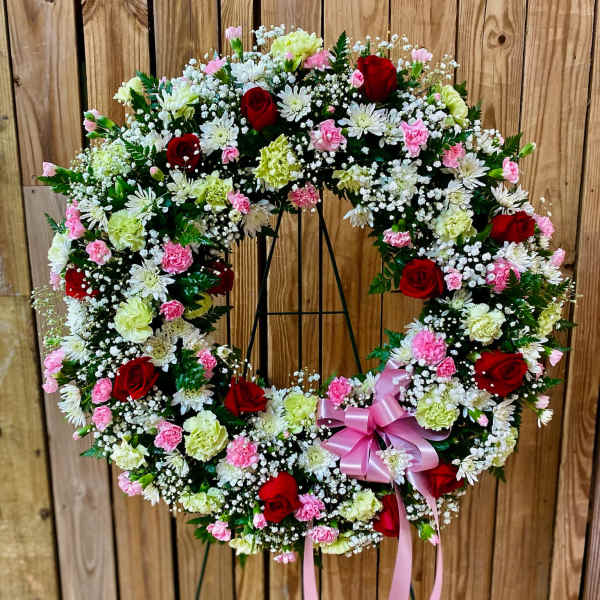 Circular floral wreath with red roses, pink carnations, and white daisies