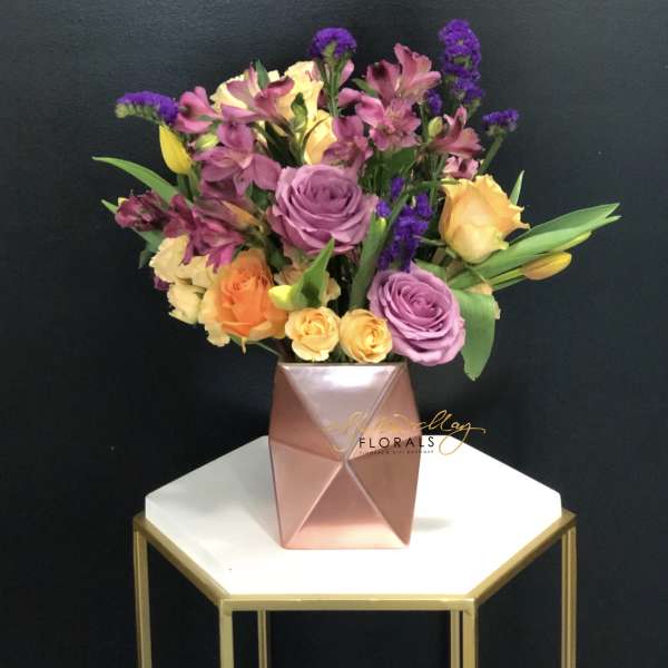 Mixed bouquet of roses and purple flowers in a pink geometric vase