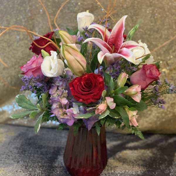 Mixed bouquet of roses, lilies, and purple flowers in a red vase
