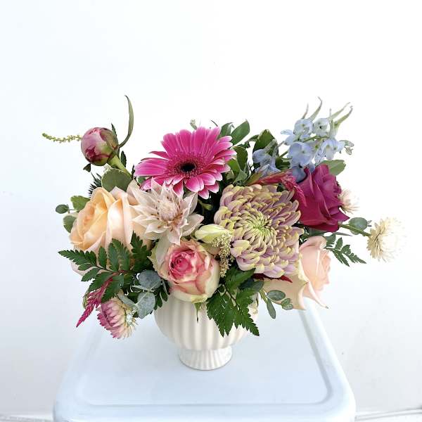 Mixed bouquet in a white vase with pink, peach, and blue flowers