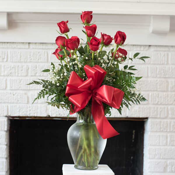 Red roses arranged in a clear glass vase with a large red bow