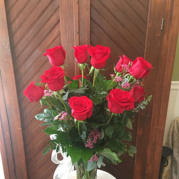 Tall vase of red roses with pink filler flowers and a white ribbon