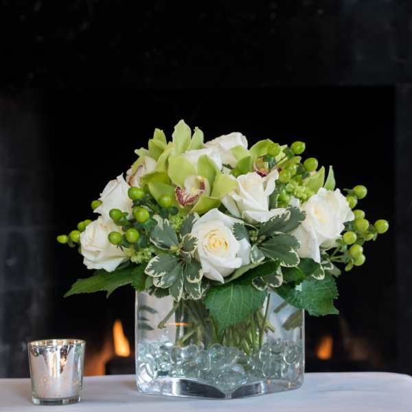 White roses and green orchids arranged in a glass vase with decorative beads.