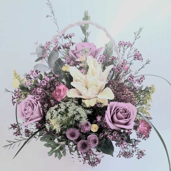 Lavender roses, cream lilies, and mixed blooms arranged in a white handled basket