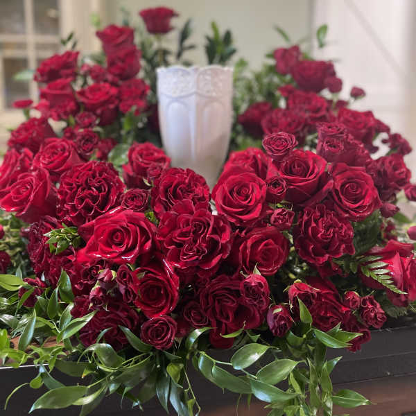 Red rose arrangement surrounding a white urn centerpiece