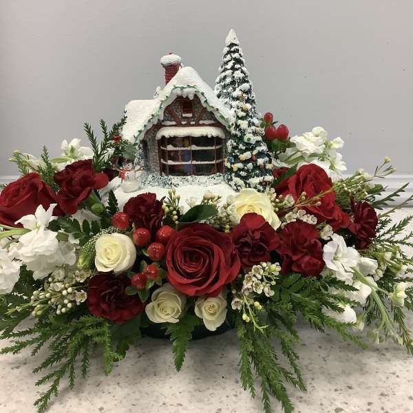 Christmas floral arrangement with red and white roses around a snowy house centerpiece