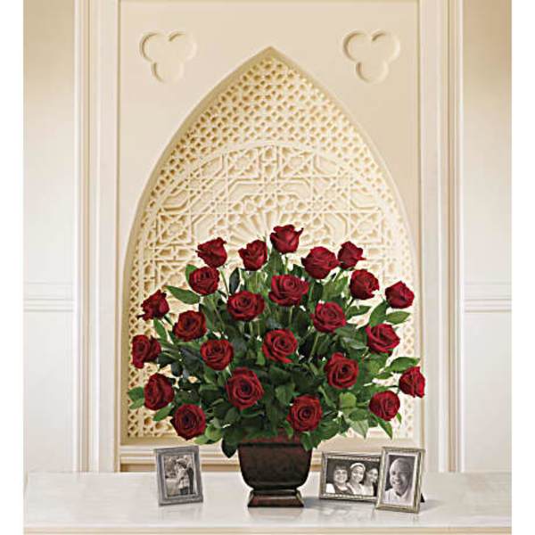 Red roses arranged in a dark vase on a table with framed photos