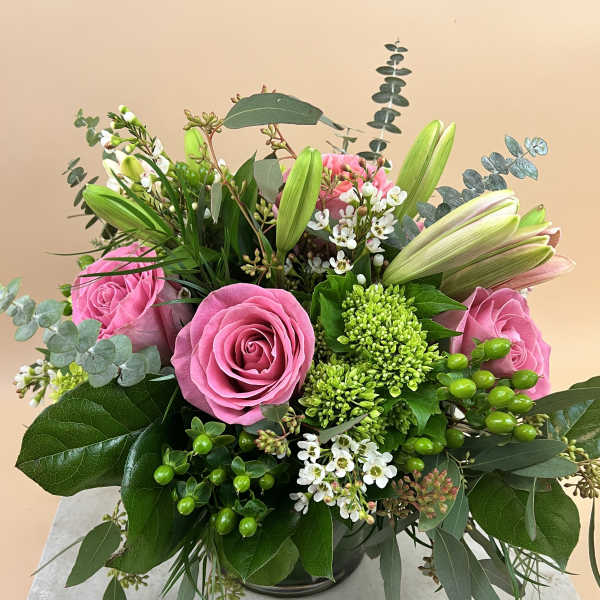 Pink roses and lilies arranged in a low vase with white filler flowers