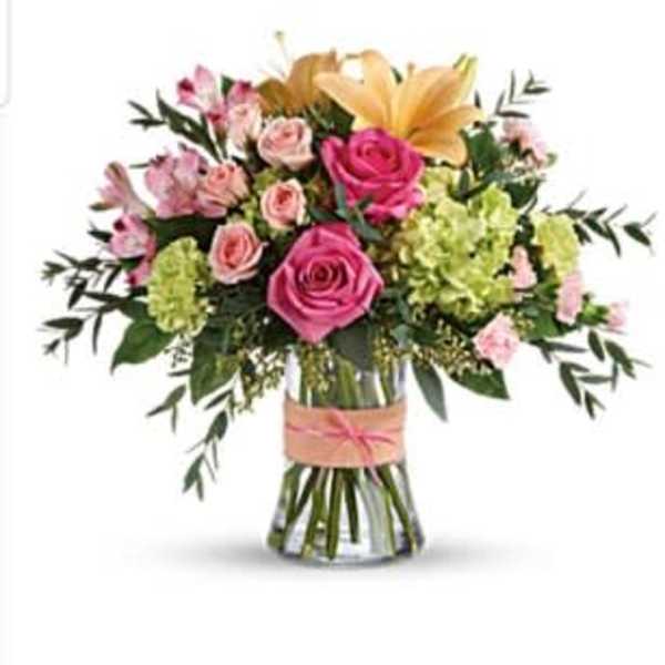 Mixed bouquet of pink roses, lilies, and green hydrangeas in a clear vase with a peach ribbon.