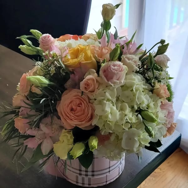 Mixed bouquet of pastel roses and hydrangeas in a plaid round box