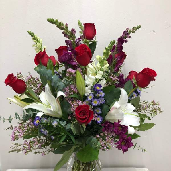 Mixed bouquet of red roses, white lilies, and purple flowers in a glass vase