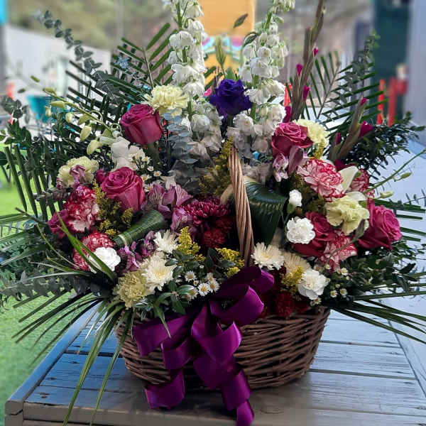 Large basket arrangement with pink roses and white flowers, tied with a purple ribbon