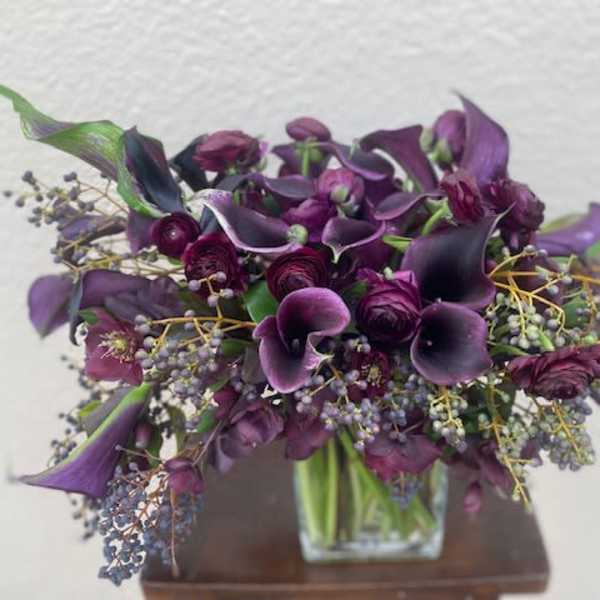 Purple calla lilies and roses arranged in a clear square vase