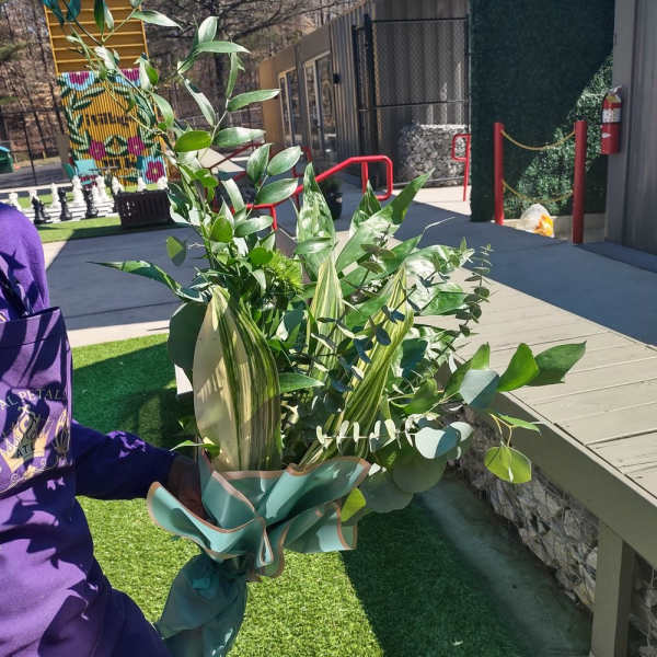 Tall bouquet of assorted green foliage wrapped in teal paper