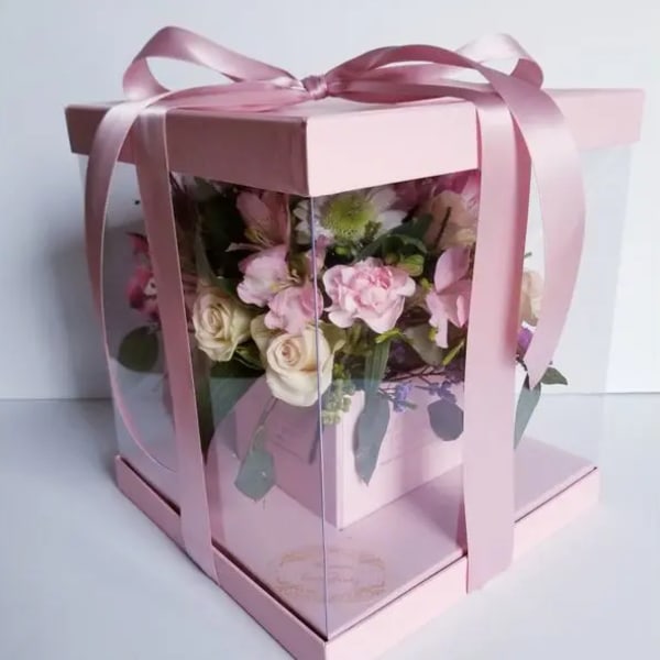Pink roses and carnations in a clear gift box with a ribbon bow