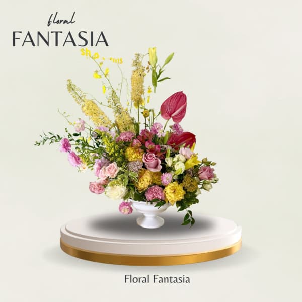 Mixed pink, yellow, and white flowers arranged in a white pedestal vase