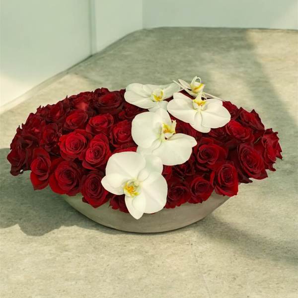 Low arrangement of red roses with white orchids in a shallow gray container