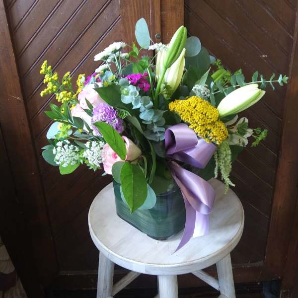 Mixed bouquet with lilies, roses, and a purple ribbon in a vase