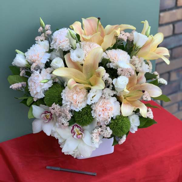 Mixed bouquet of lilies, carnations, and orchids in a white container