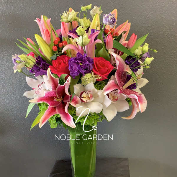 Tall bouquet of pink lilies, roses, and orchids in a glass vase