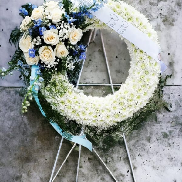 White floral funeral wreath with roses and blue accents on a stand