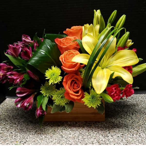 Mixed bouquet with yellow lilies, orange roses, and purple alstroemeria in a wooden box