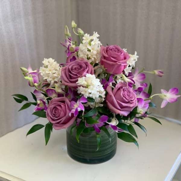 Pink roses and purple orchids arranged in a green glass vase