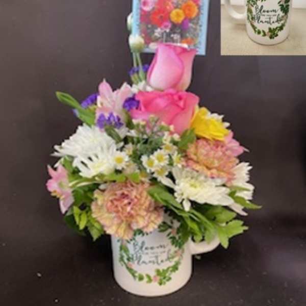 Colorful mixed flower arrangement in a white mug with floral print and an attached flower seed packet.