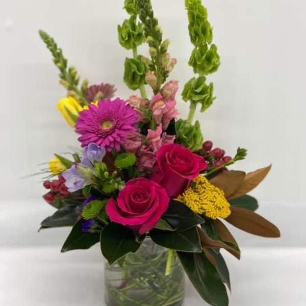 Mixed bouquet with pink roses, purple daisies, and tall green spikes in a glass vase