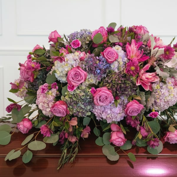 Large pink and lavender floral arrangement on a wooden casket