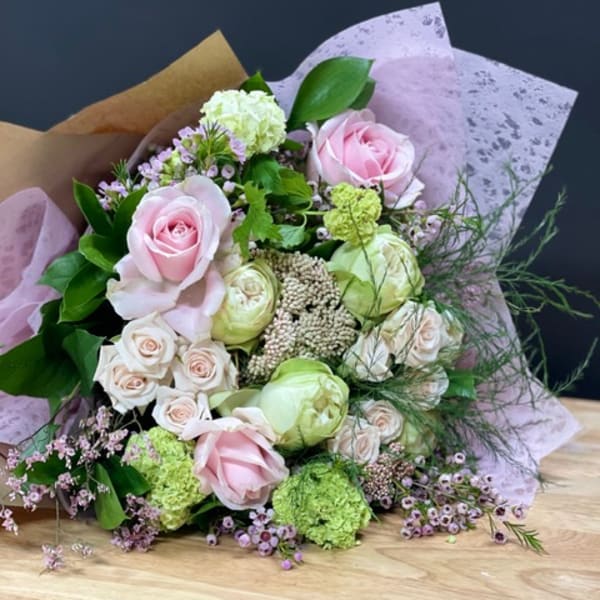 Bouquet of pale pink and cream roses with green blooms wrapped in lavender paper