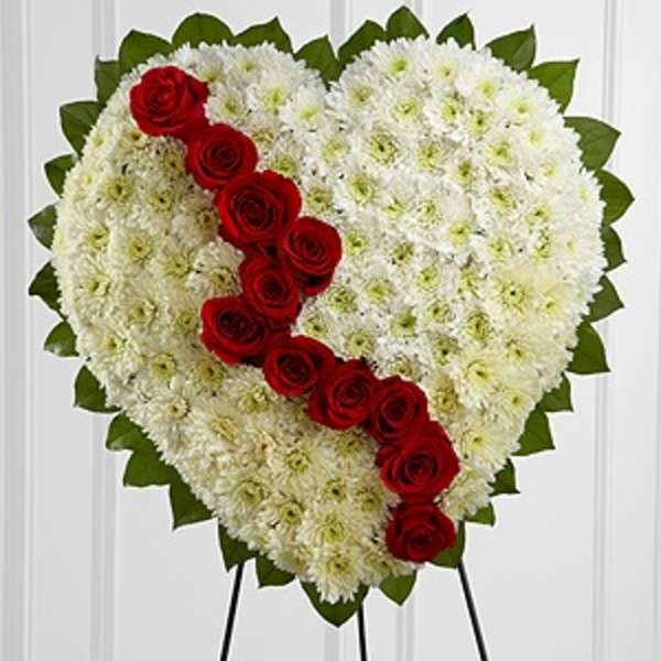 Heart-shaped floral tribute with red roses and white flowers on an easel