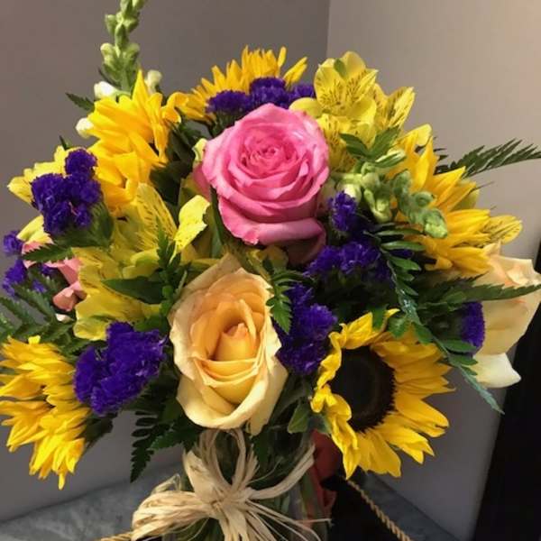 Bouquet of pink and peach roses with yellow sunflowers and purple filler flowers
