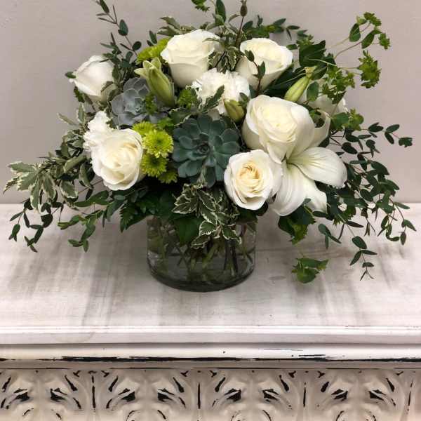 White roses and lilies in a glass vase with green succulents and foliage