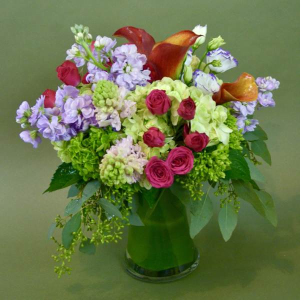 Mixed bouquet with pink roses, purple blooms, and orange calla lilies in a glass vase