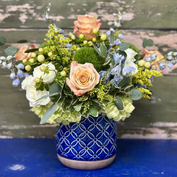 Mixed bouquet of peach roses, white blooms, and blue flowers in a patterned blue vase