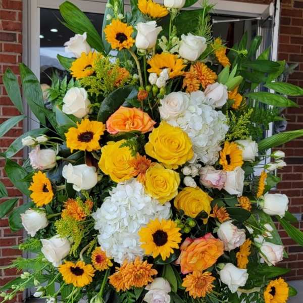 Tall standing spray of yellow roses, sunflowers and white roses with hydrangeas on an easel.
