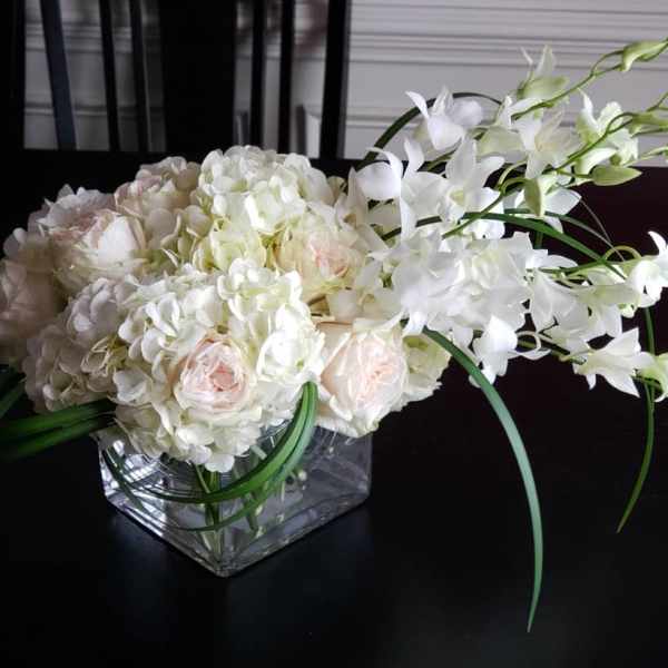 White and pale pink floral arrangement in a square glass vase