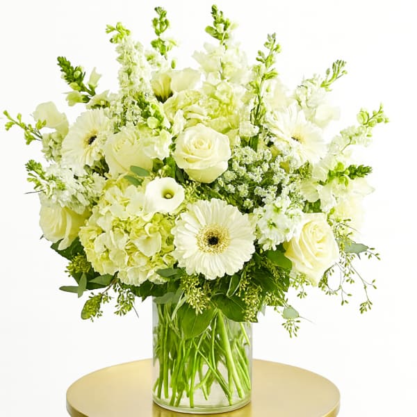 White floral arrangement in a clear glass vase on a gold table