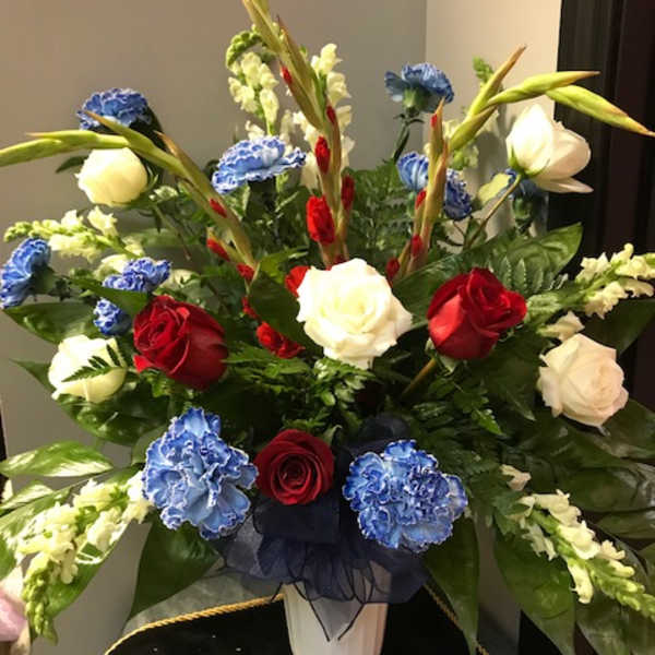 Red, white, and blue floral arrangement in a white pedestal vase