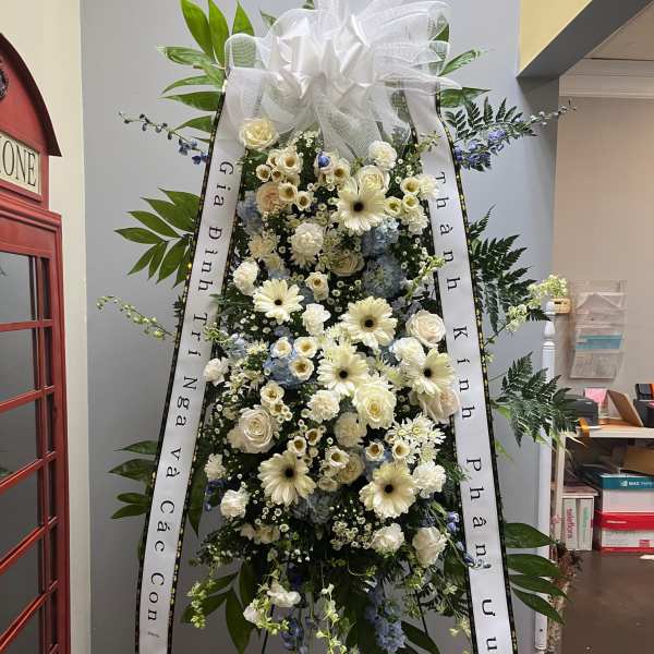 Standing funeral spray of white and pale blue flowers with ribbons