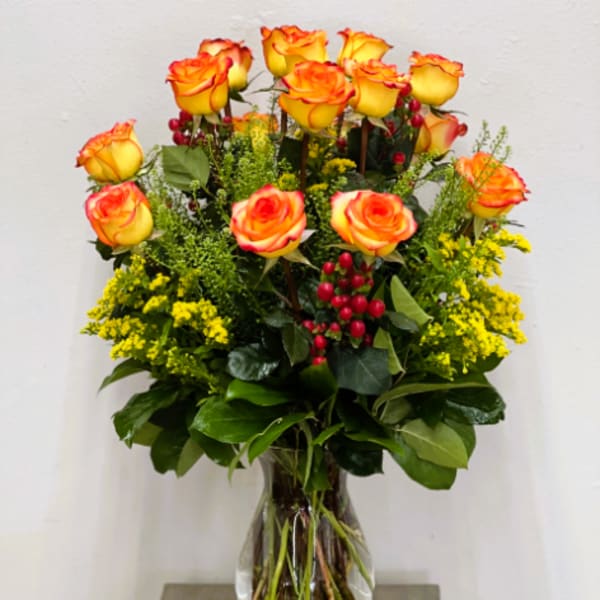 Yellow-orange roses in a clear glass vase with red berries