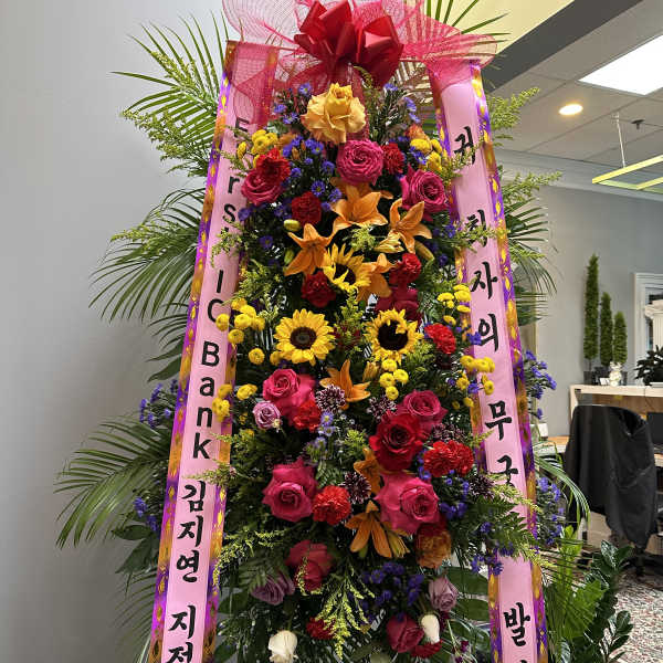 Tall standing floral wreath with pink ribbons and mixed blooms