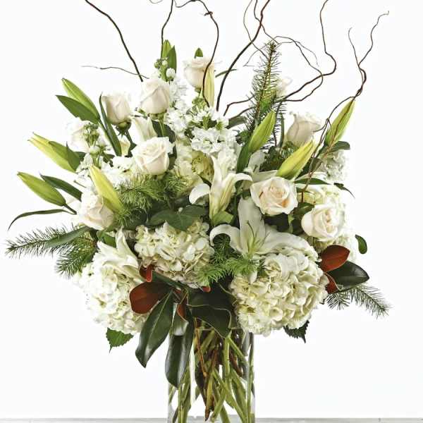 White roses and lilies in a clear glass vase with curly branches