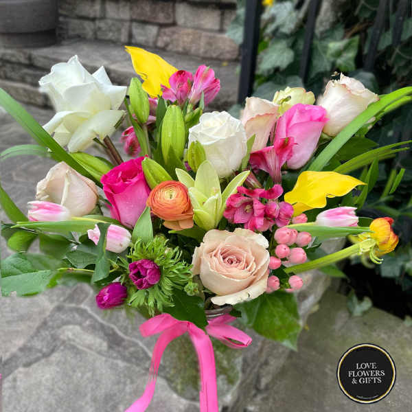Mixed bouquet of pink, white, and yellow flowers in a glass vase with a pink ribbon