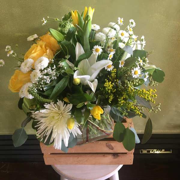 Yellow and white mixed bouquet in a glass vase with a wooden crate